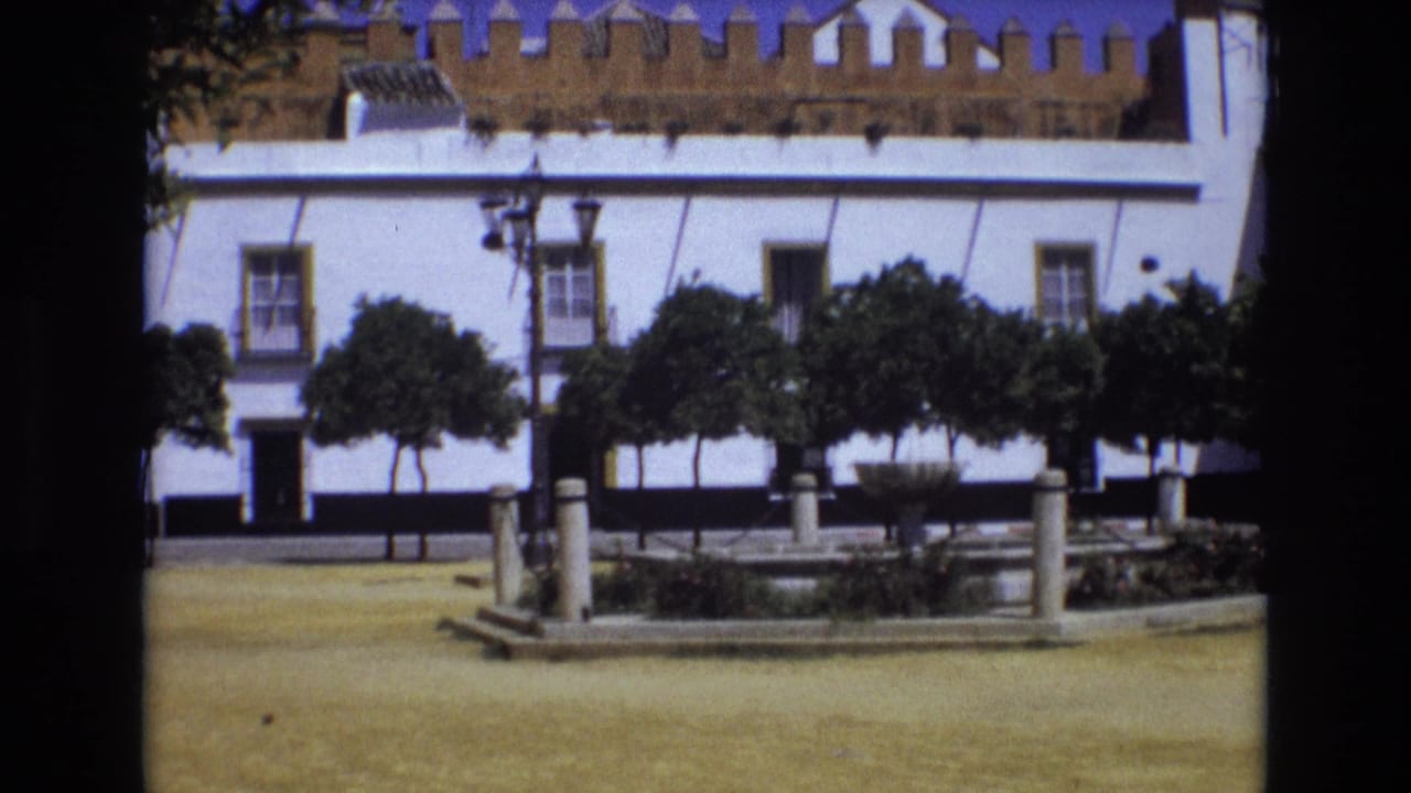 Town square with white building, trees, fountain, and stone posts.