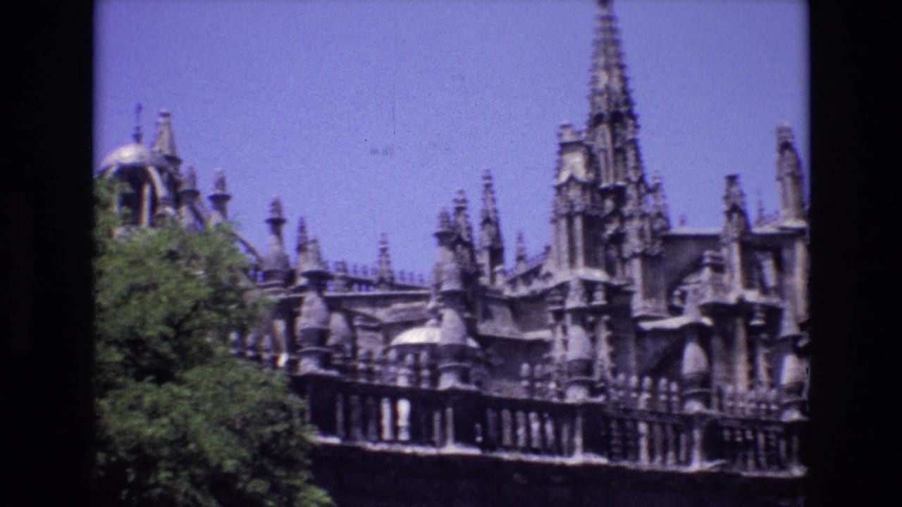 Stone spires and pinnacles above a balustrade with trees at the left edge.