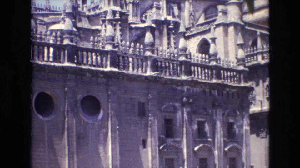 1972 Spain home-movie view of a historic cathedral facade, with circular windows below a stone balustrade and dense spires above.