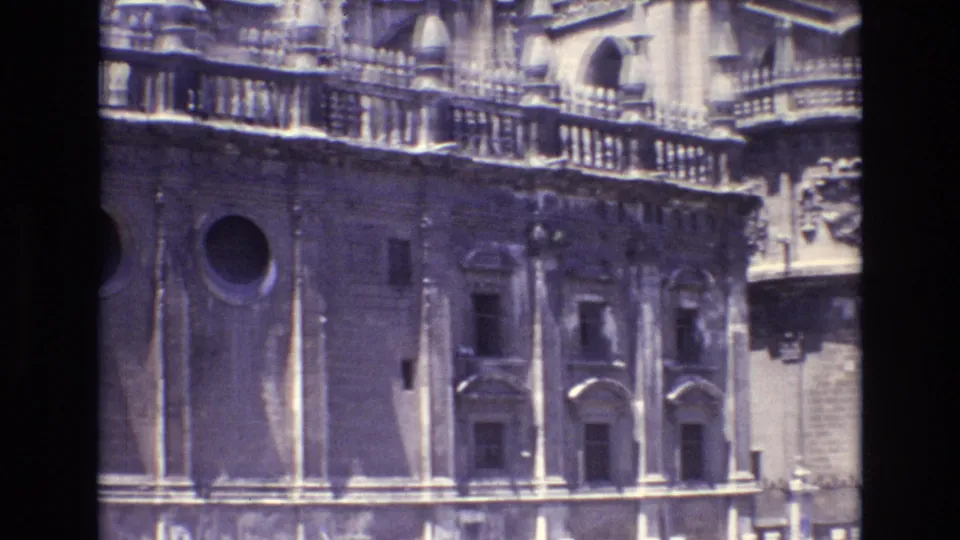 1972 Spain 8mm frame from a downward pan across a cathedral facade, showing a round window, small arched doors, vertical stone elements, and ornate upper railings.