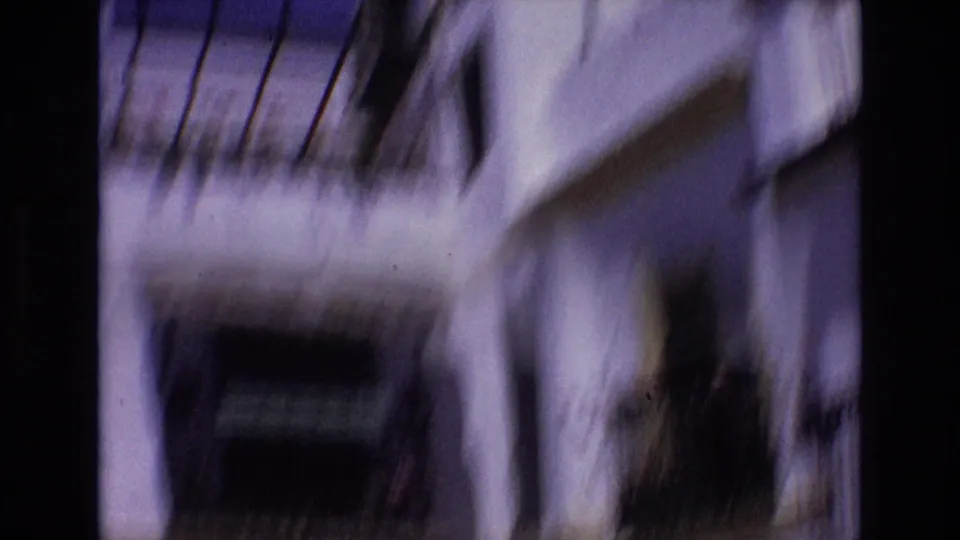 1972 Spain 8mm frame with strong handheld motion blur across a whitewashed facade, dark wrought-iron balcony railings, and shadowed architectural openings.