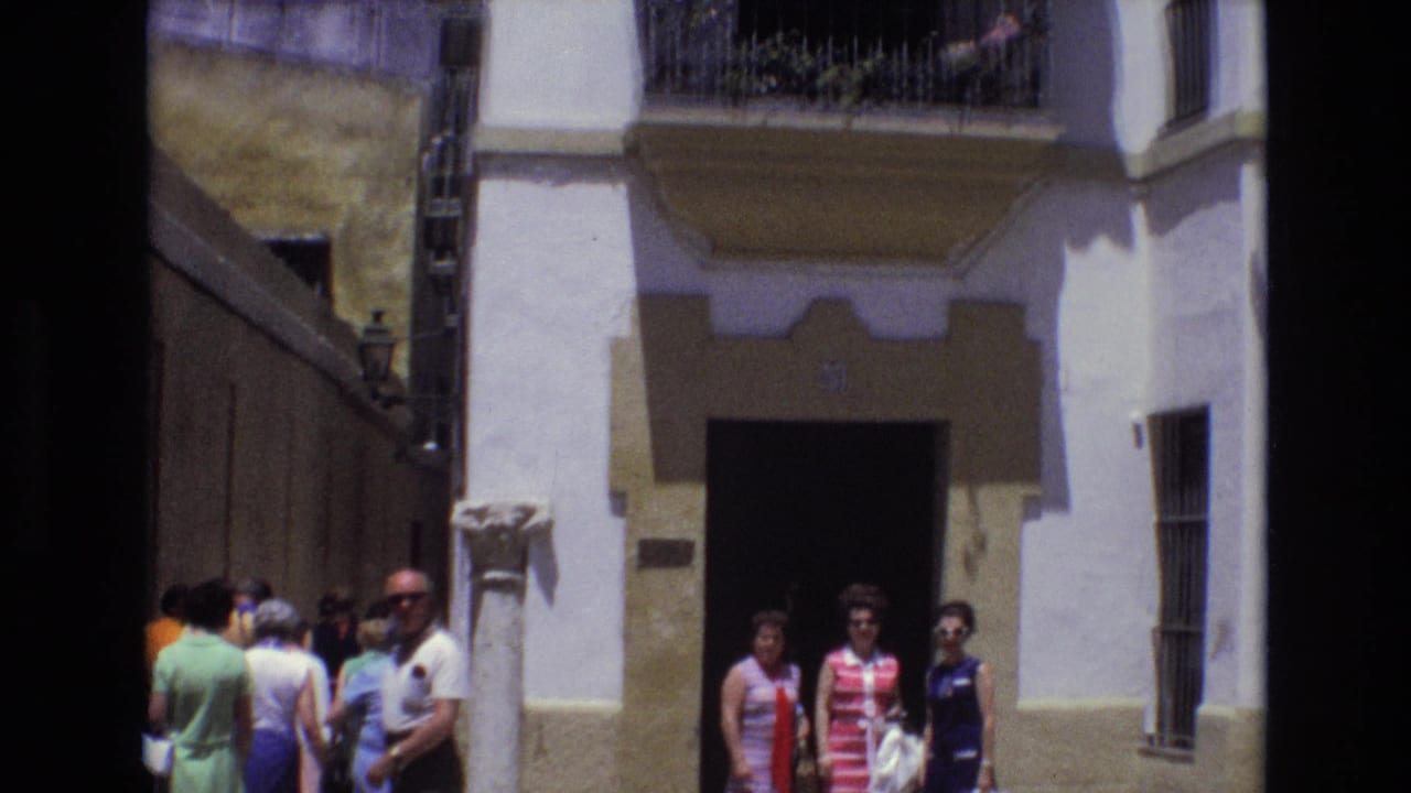 People standing and walking near a white building entrance on a narrow street.