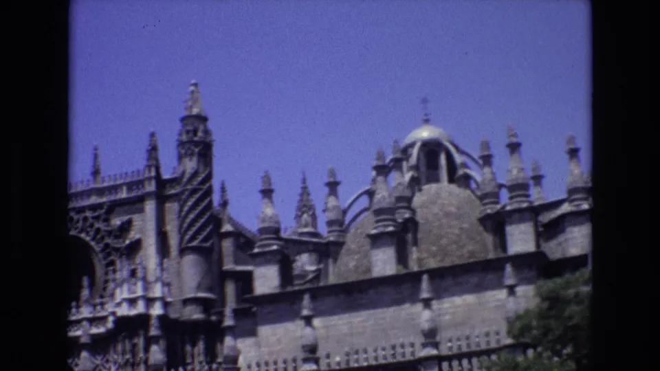 1972 Spain home-movie frame with the camera on ornate stone roofline details, including spires, carved Gothic elements, and a rounded dome feature.