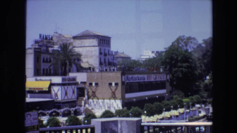 1972 Spain home-movie frame of a waterfront commercial area with visible HAMSA and Restaurante RIO GRANDE signage, trees, awnings, railings, and outdoor seating.