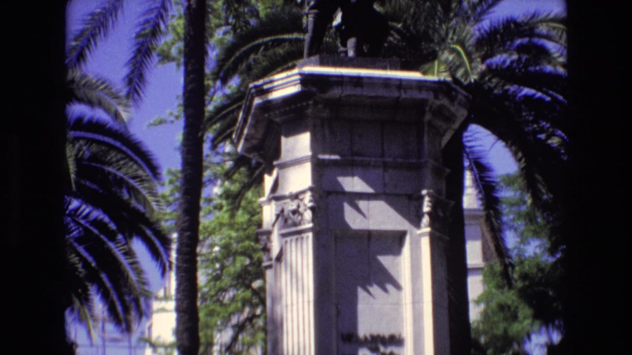 Stone monument pedestal with carved details, palm trees, and deep sun shadows.