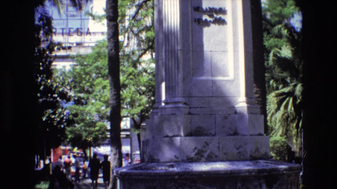 Monument base and columns with trees, palms, and small pedestrians visible beyond.