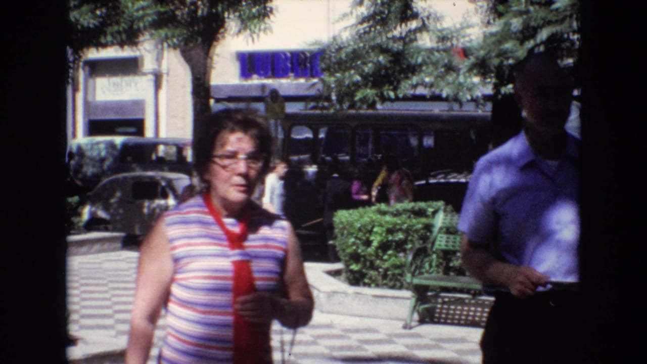 Woman in a striped sleeveless top walks across a sunny plaza near a man in shadow.