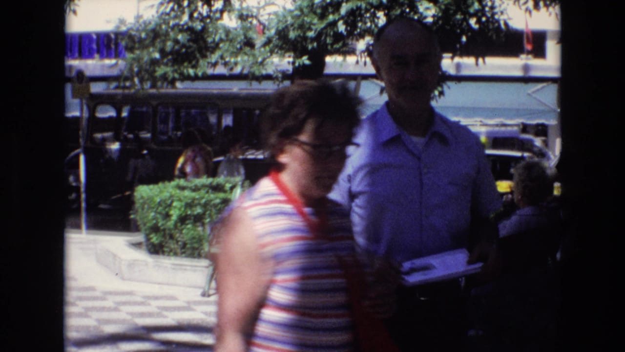 Woman passes close to the camera as a man holds papers near the plaza edge.