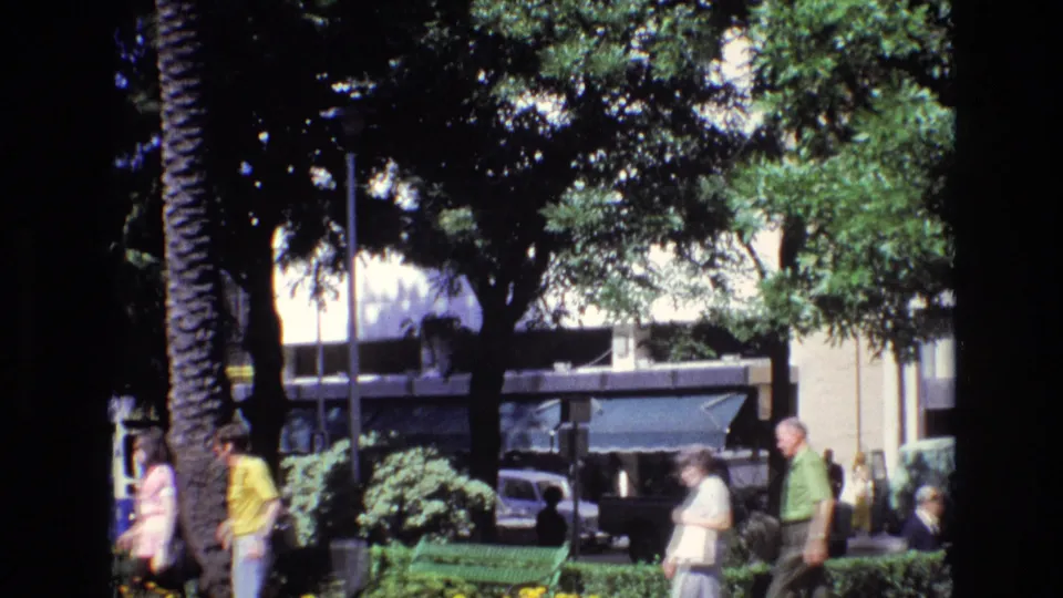 The final frame shows a Spanish urban plaza around 1972 with pedestrians near green benches and trees, while older cars, a bus, and commercial building fronts sit in the bright background.