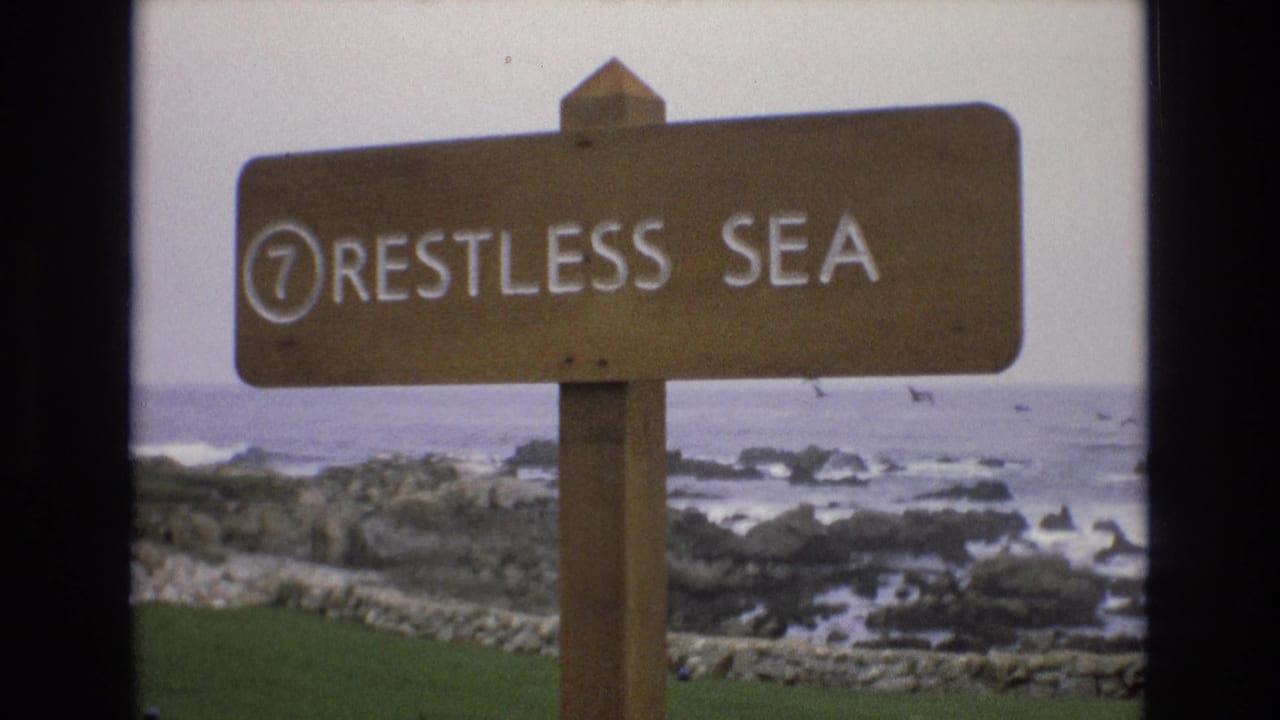 Wooden sign reading 7 RESTLESS SEA beside a rocky ocean shoreline.