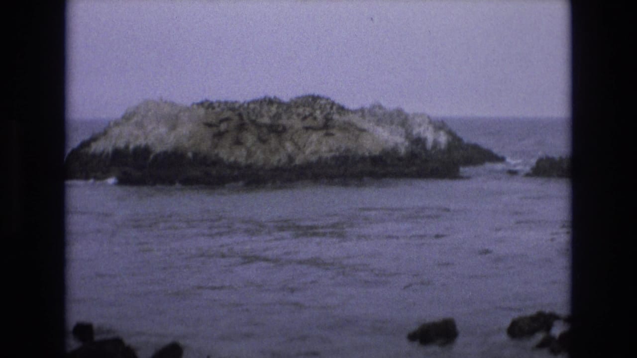 Offshore rock centered across calm water under a pale sky.
