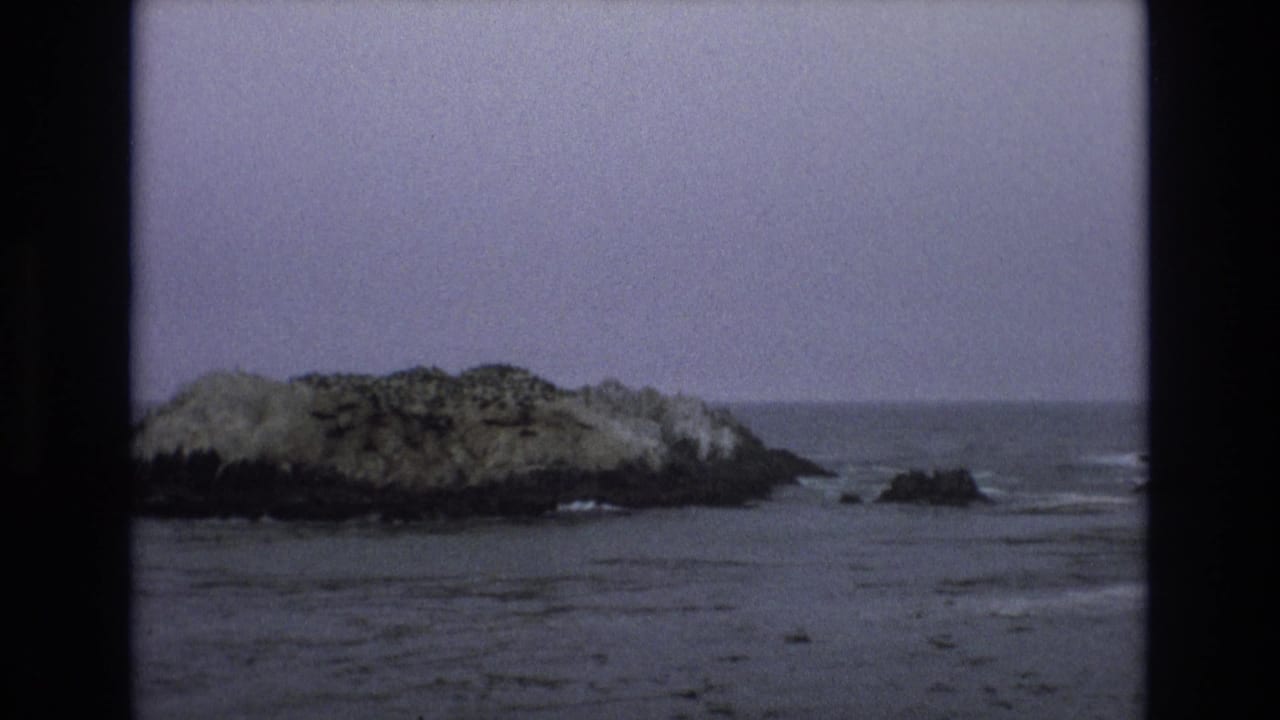 Rocky offshore islet surrounded by calm ocean water under a pale sky.