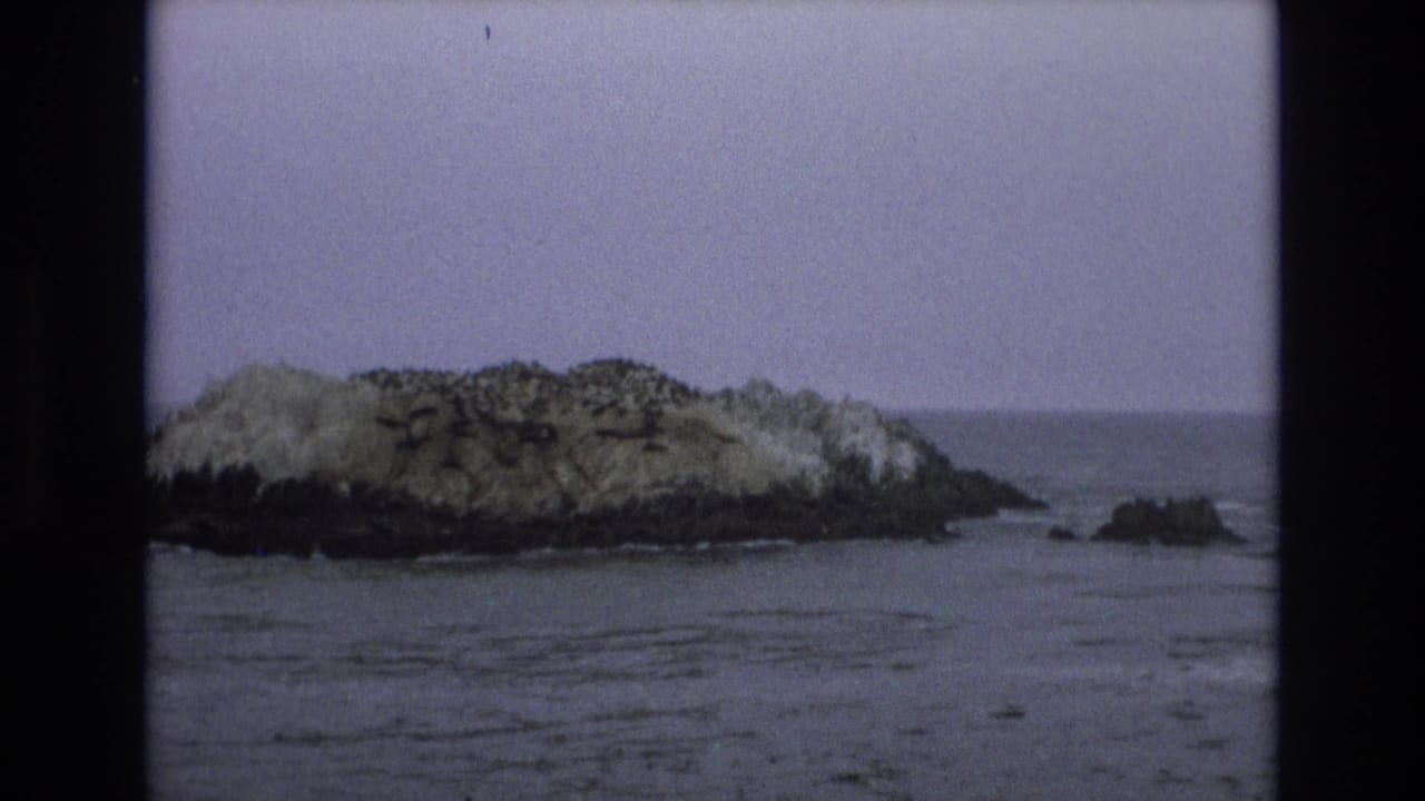 1973 8mm Central Coast California view of a rugged islet with a smaller rock outcrop nearby and soft waves around the base.