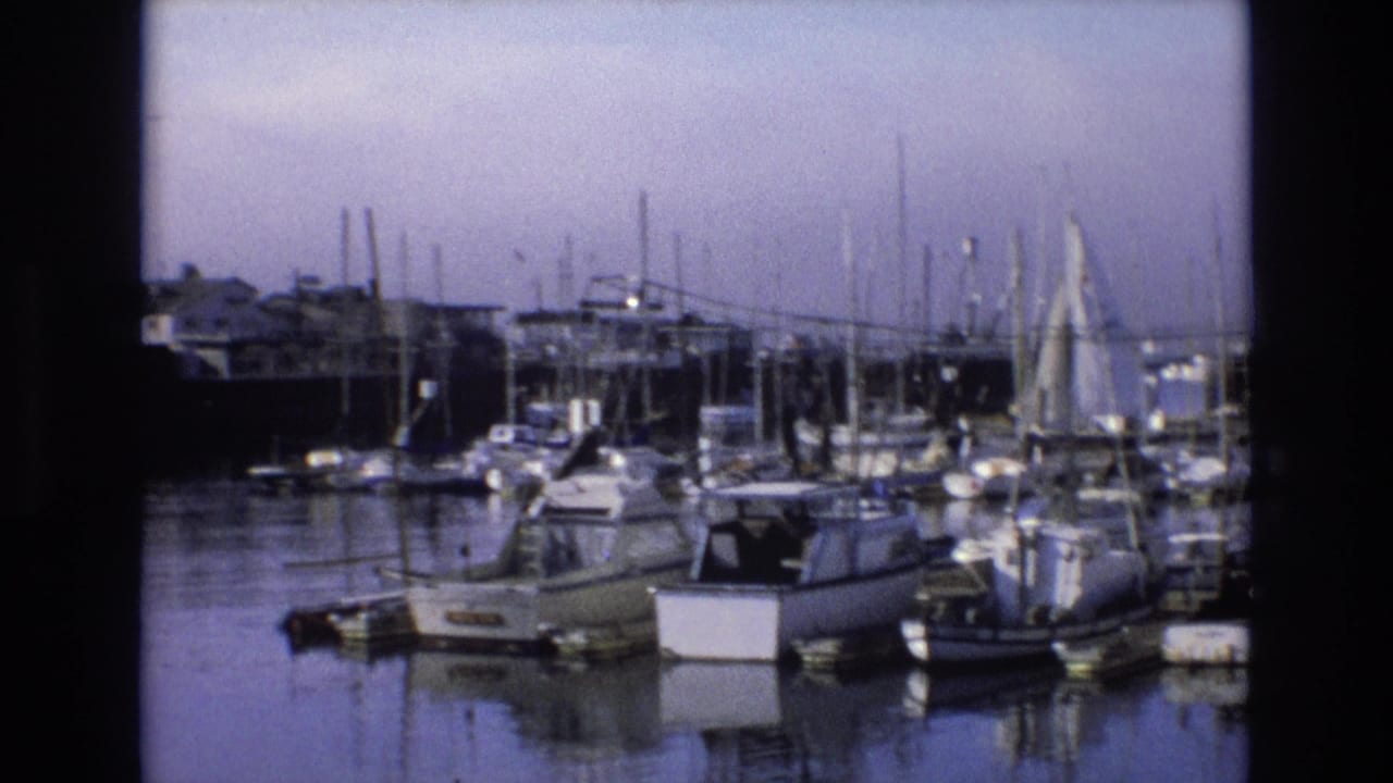 1973 California coastal home-movie frame showing sailboats and motorboats moored in a marina under a hazy sky.