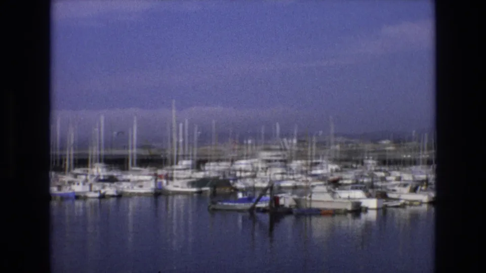 1973 Central Coast California 8mm frame showing a marina filled with docked sailboats and yachts, with vertical masts against a hazy blue-purple sky.