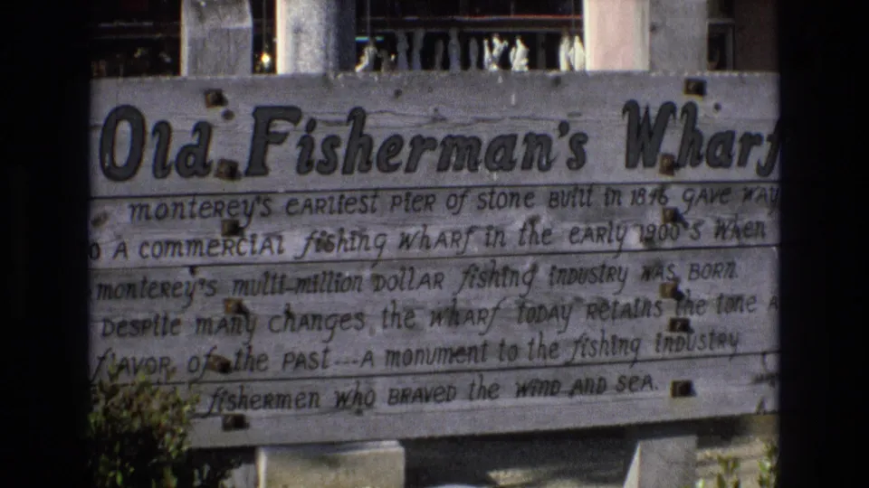 1973 Central Coast California 8mm frame showing a weathered Old Fisherman's Wharf sign describing Monterey's early stone pier and fishing wharf history.