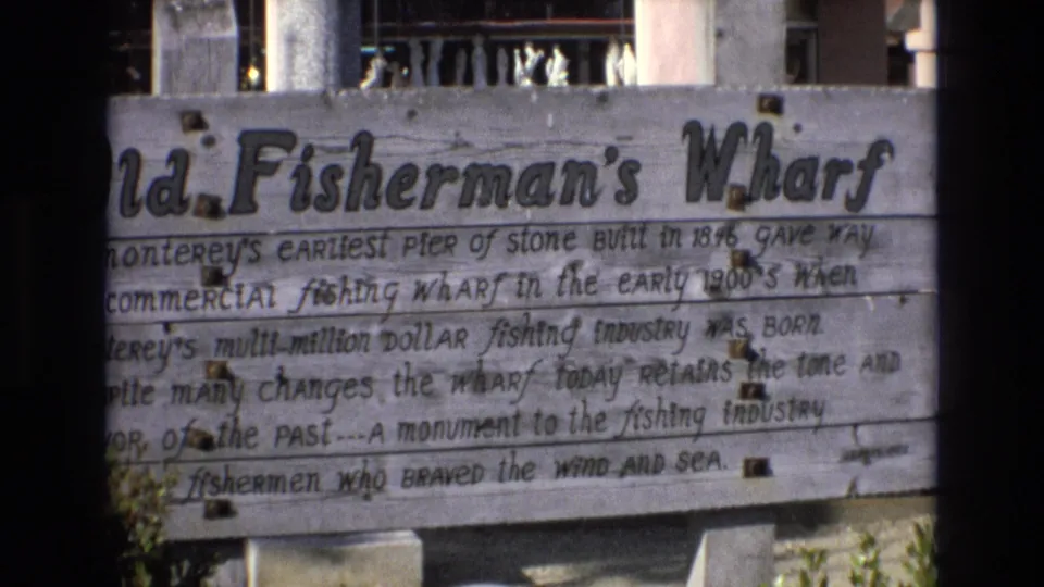 1973 Central Coast California visitor-shot frame lingering on the Old Fisherman's Wharf sign, with weathered boards and partially readable text about Monterey's fishing past.