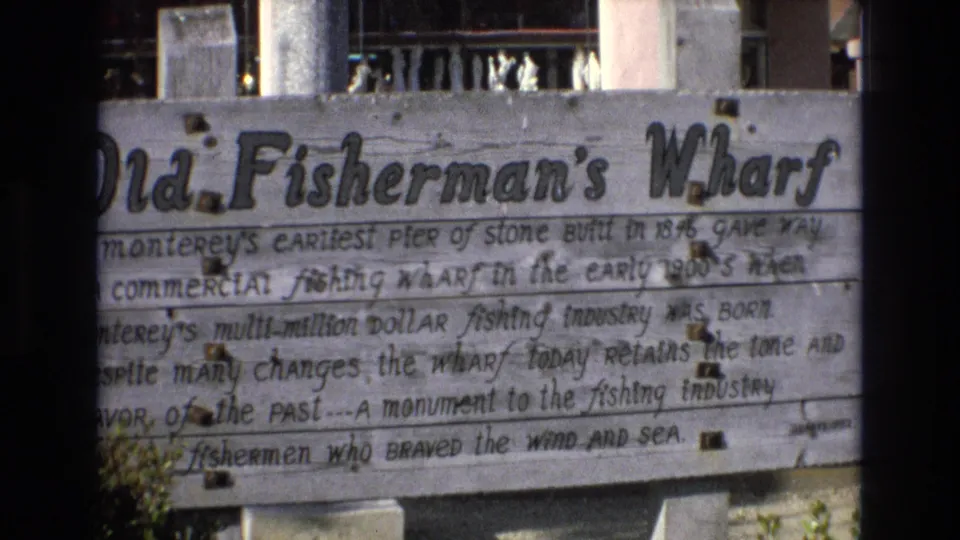 Handheld 1973 8mm frame of the Monterey Old Fisherman's Wharf sign, cropped tightly across the title and text on weathered horizontal boards.