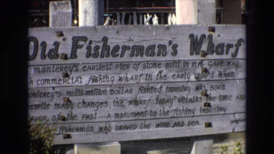 Final 1973 8mm frame of the Old Fisherman's Wharf sign at Monterey, with the title, weathered text, planked surface, and partial structure behind it visible.