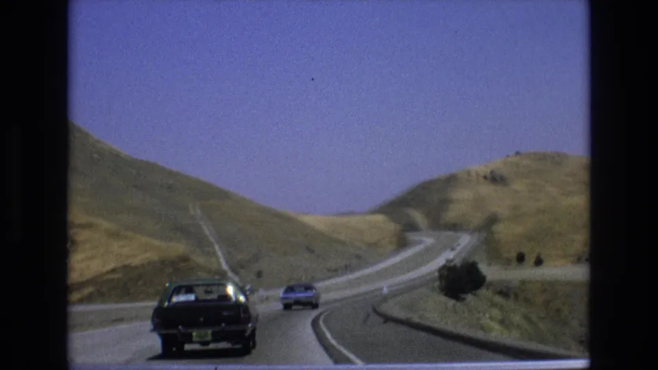 1973 Central Coast California road scene showing period cars on a winding highway cutting through dry golden hills under a blue sky.