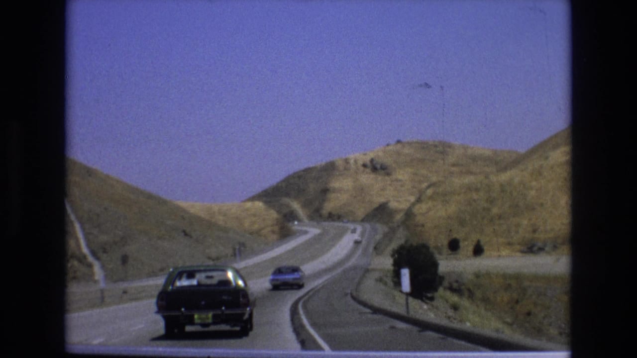 Black sedan and blue car driving on a curving highway through dry hills.