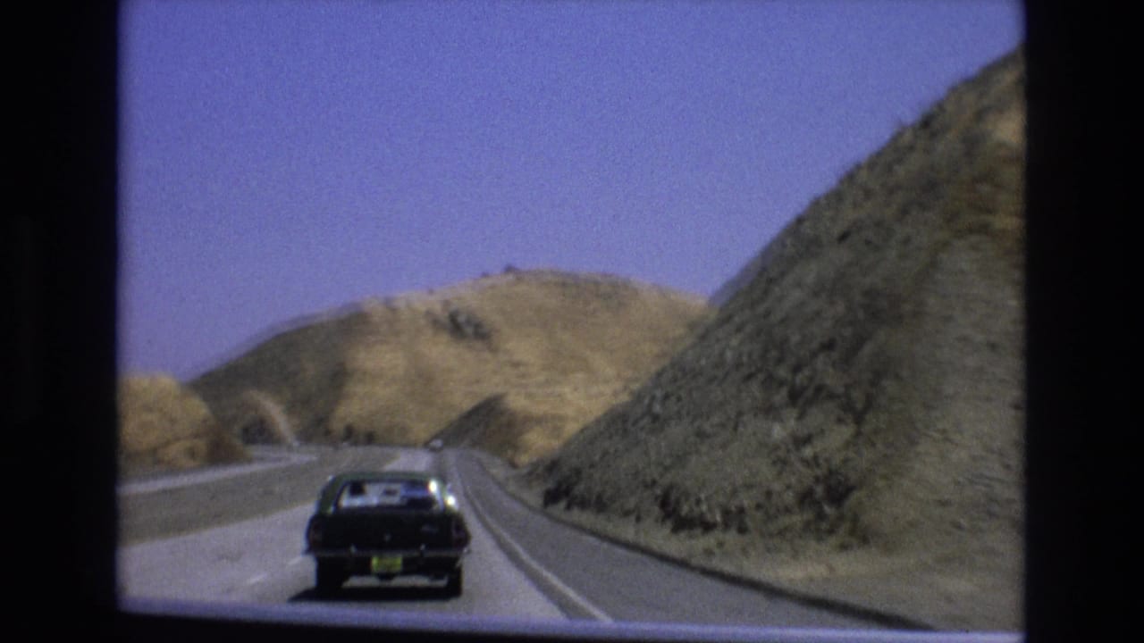 Dark car approaching a curve on a road through dry hills.