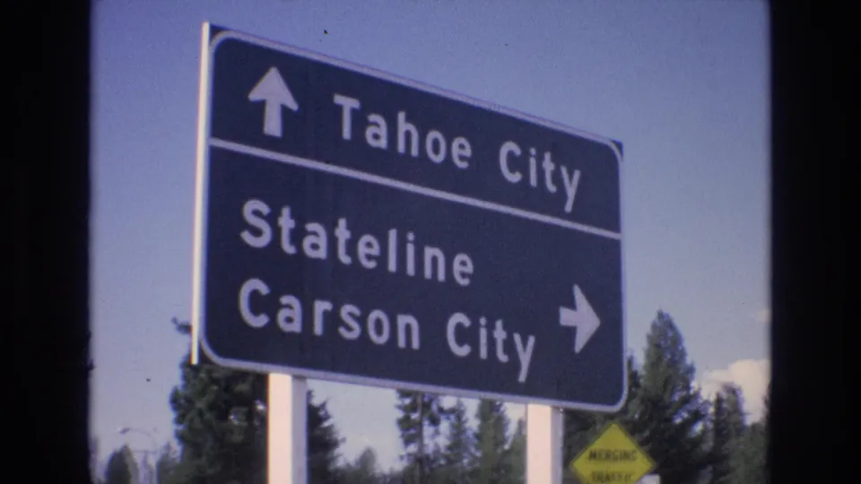 A large blue directional sign lists Tahoe City straight ahead and Stateline and Carson City to the right, filmed against sky and trees in a 1973 travel shot.