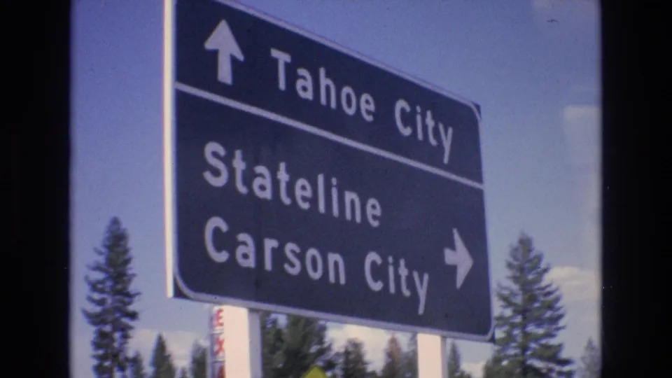 The directional road sign fills more of the frame, showing arrows and place names for Tahoe City, Stateline, and Carson City with trees and sky behind it.