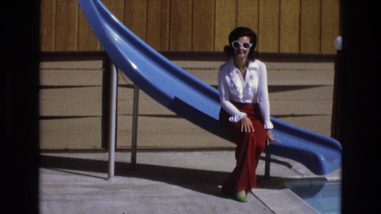 Woman remains seated at the base of a blue pool slide in bright sunlight.