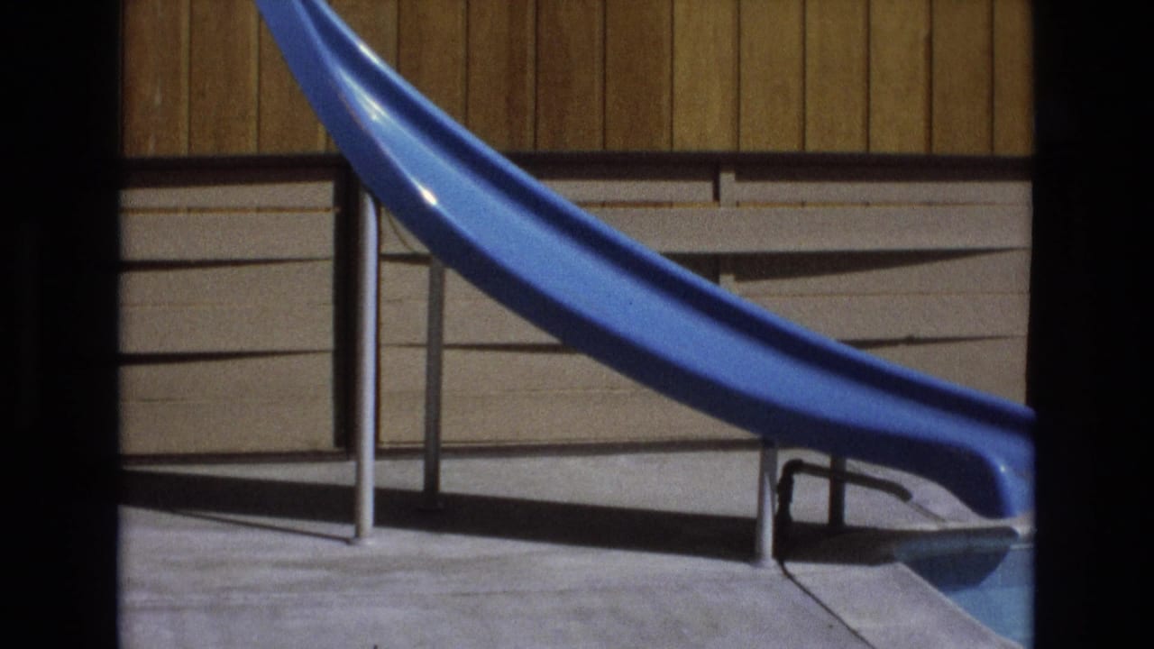 Blue slide and metal supports beside a pool with wood paneling behind.