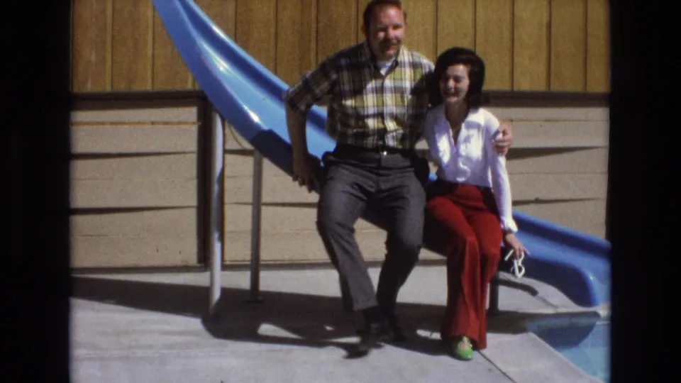 The adult couple sits close together on the blue slide, with the man’s arm around the woman in a brief affectionate pose.