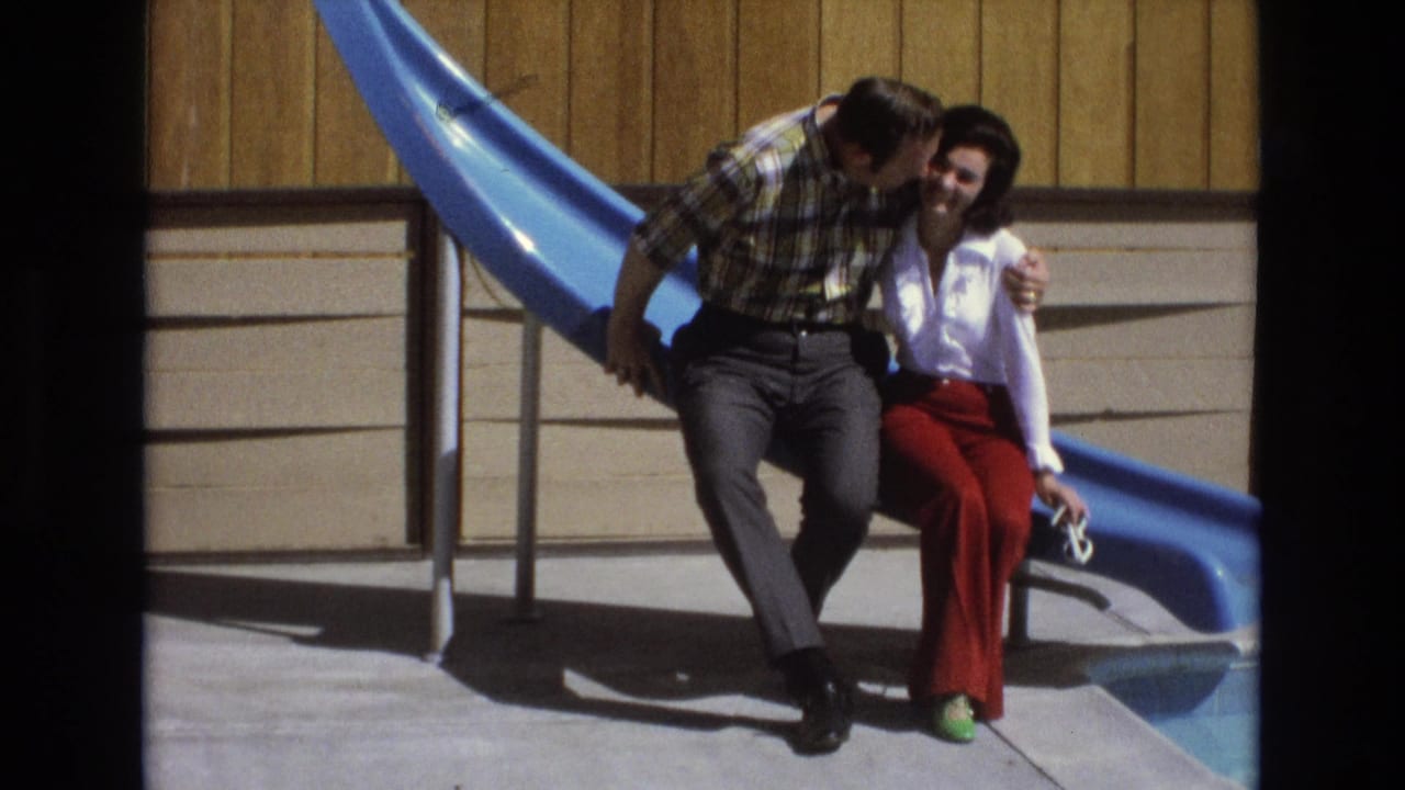 Man and woman sit close together on a bright blue slide as he leans toward her.