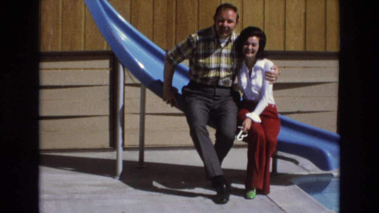 Smiling couple sits side by side on a blue slide with the man's arm around the woman.