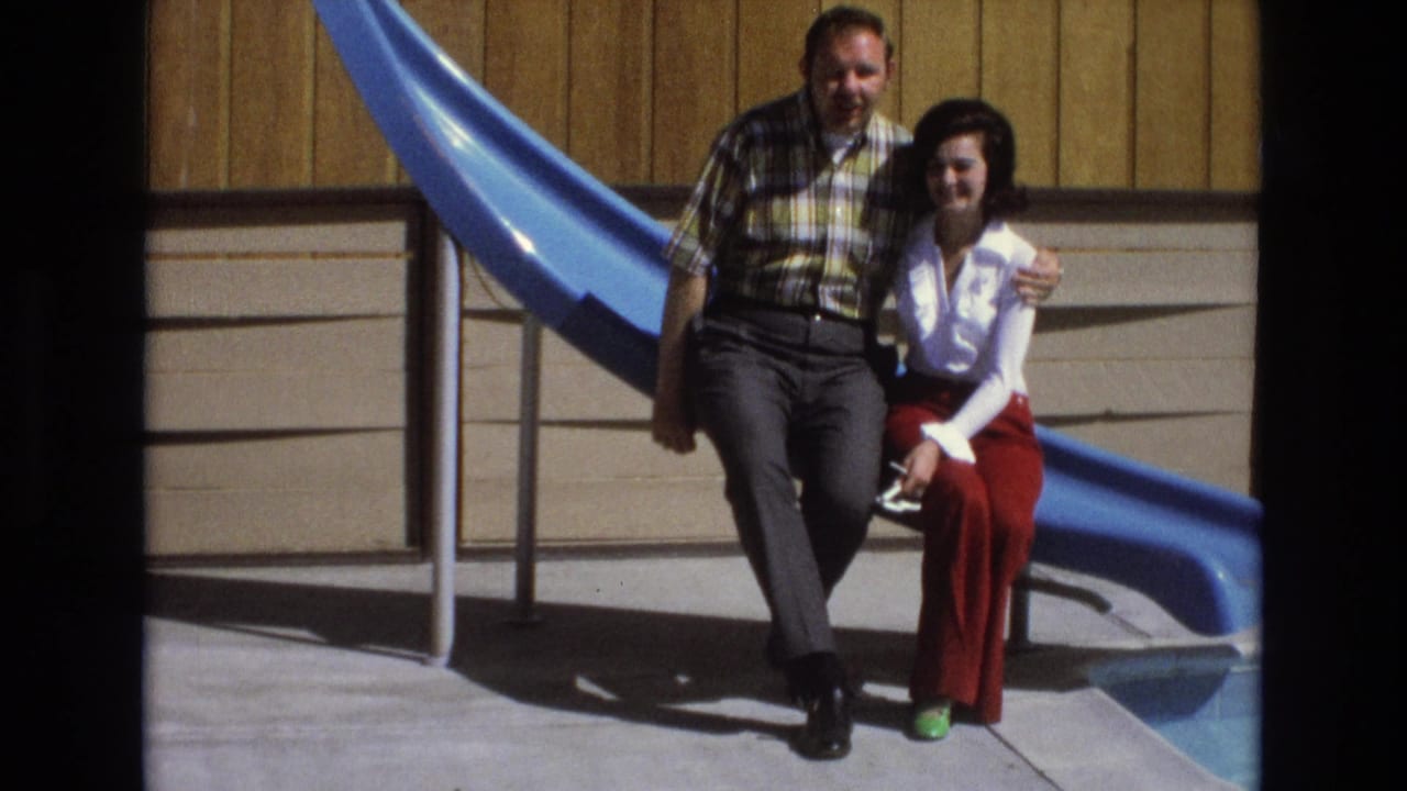 Couple seated together by a blue slide with the man's arm around the woman.