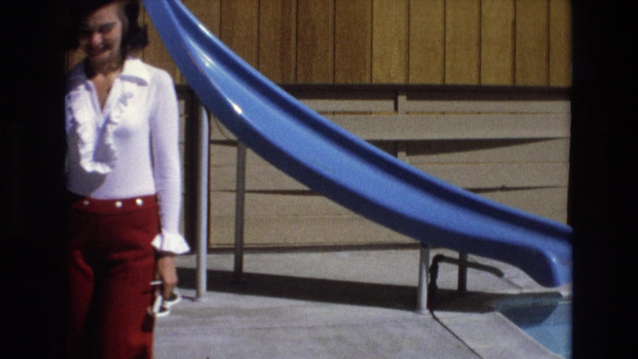 Woman in red pants and white blouse walking beside a blue pool slide.