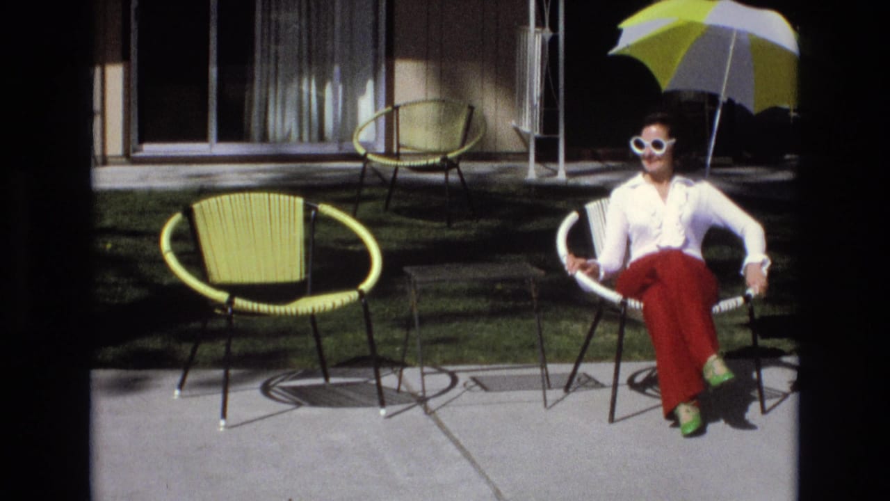 Woman sits in a patio chair under a striped umbrella with yellow outdoor furniture nearby.