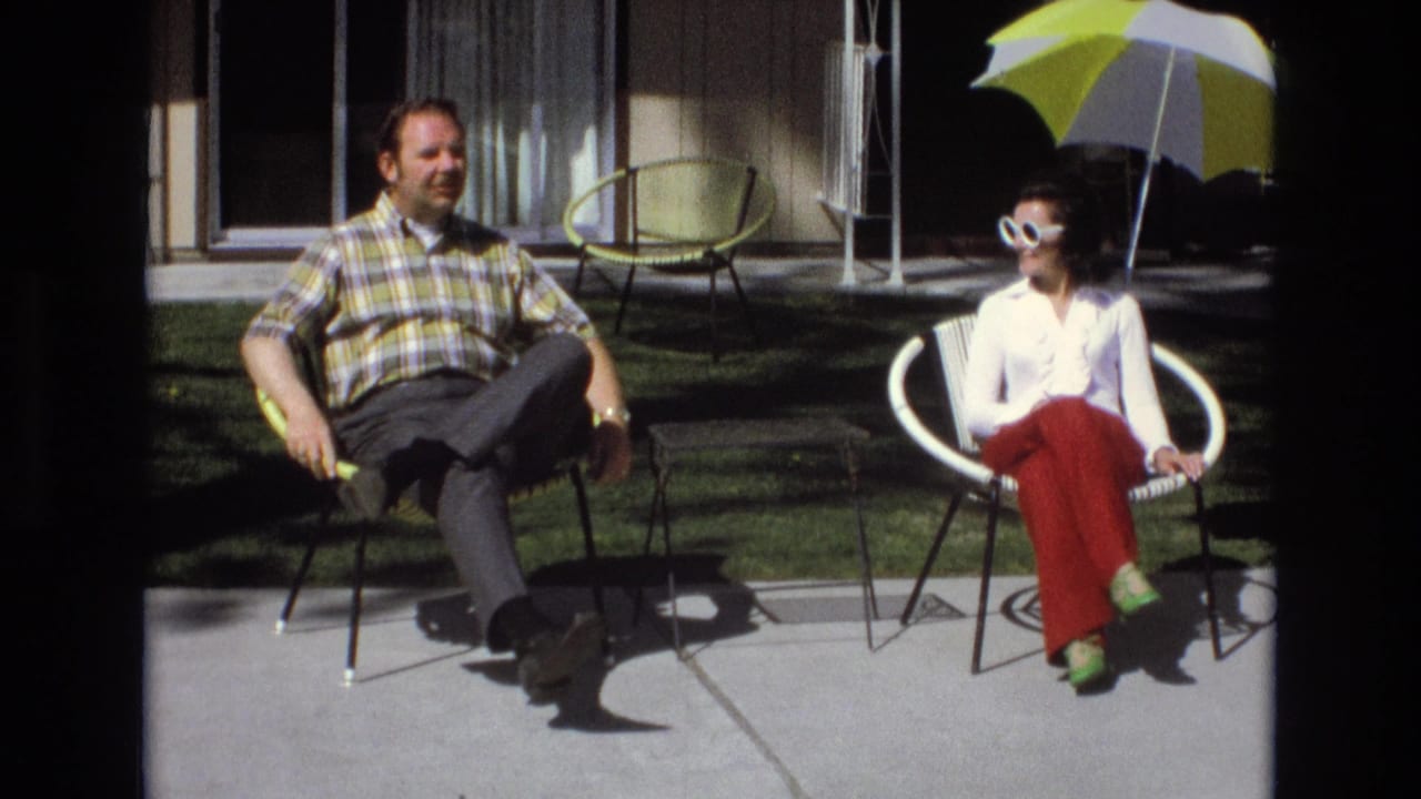 Man and woman seated on a sunny patio beside a yellow-and-white umbrella.