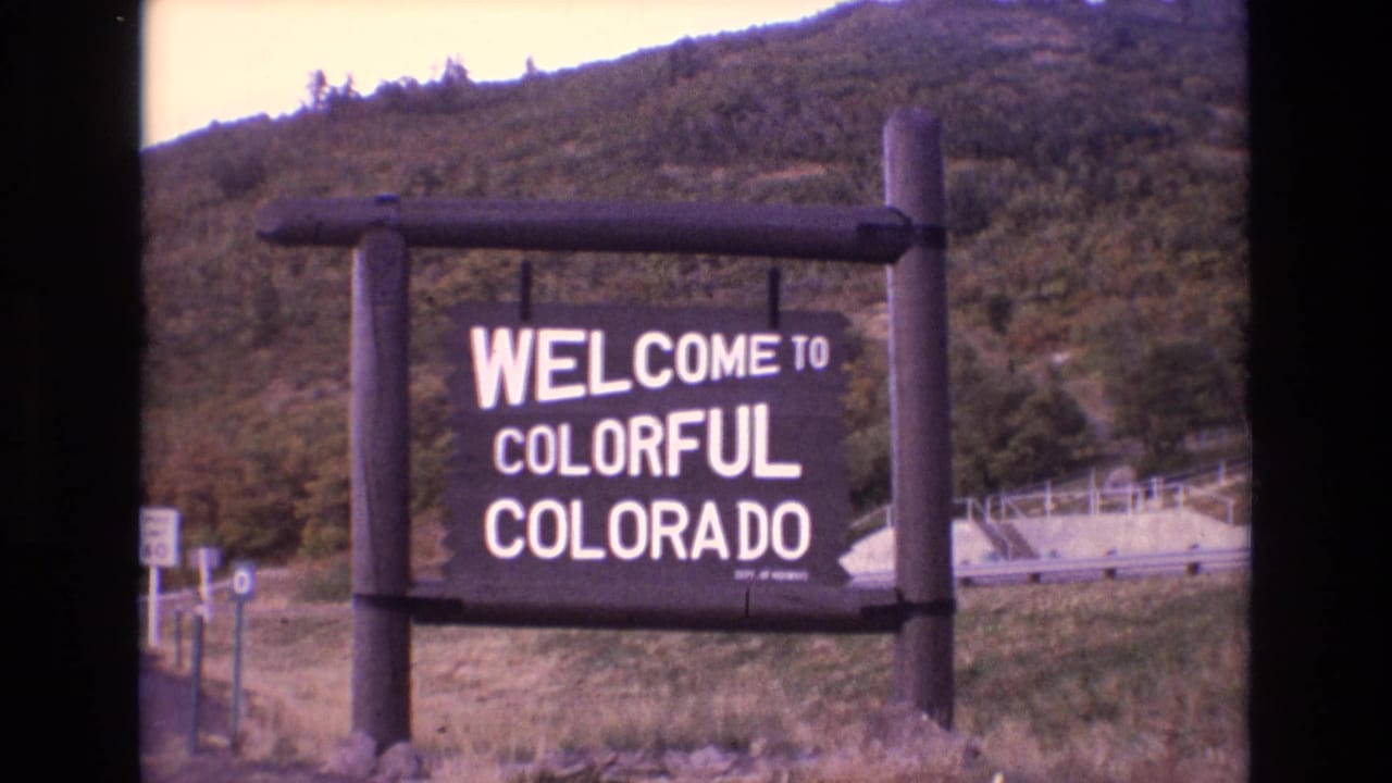 Welcome to Colorful Colorado sign framed by timber posts and hillside vegetation.
