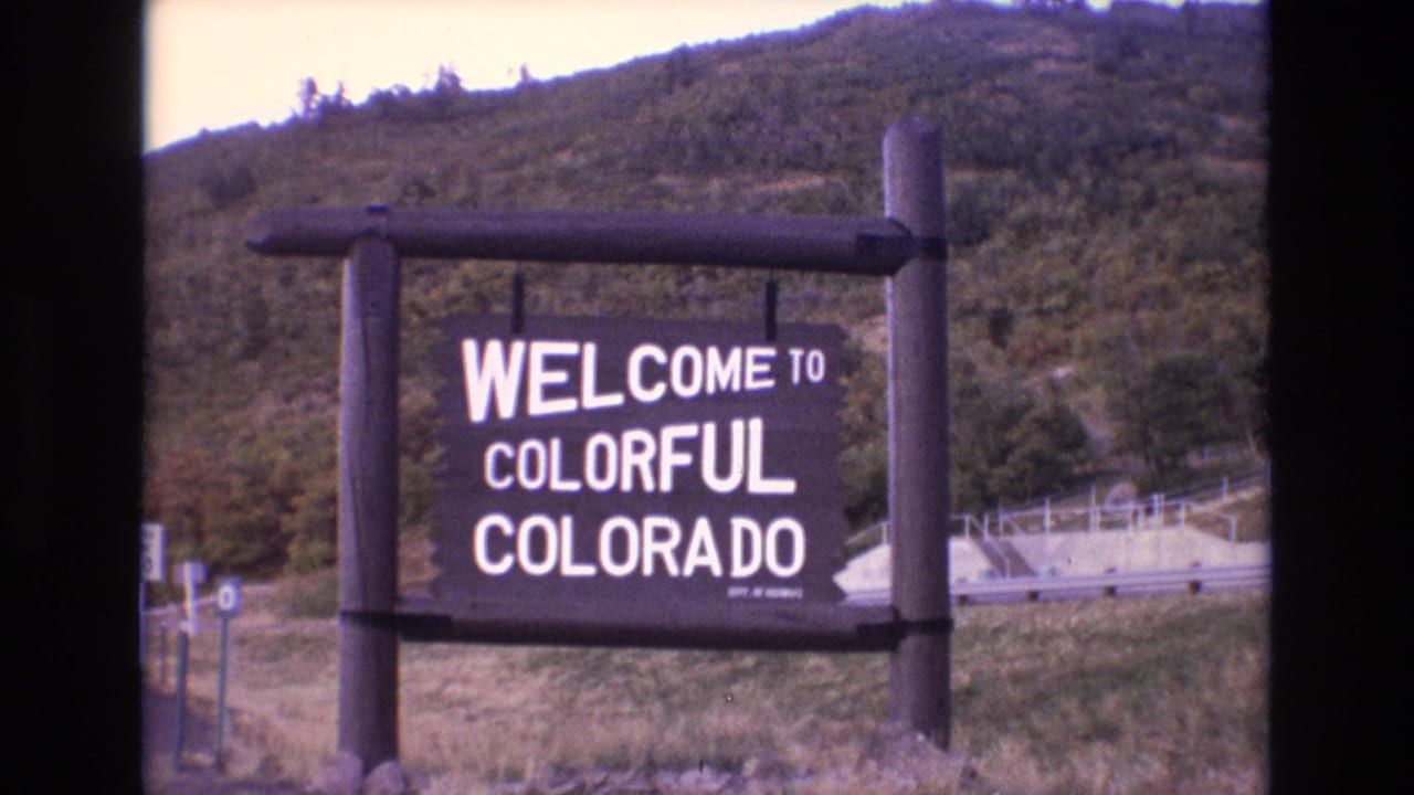 Wooden Welcome to Colorful Colorado sign beside a mountain road.