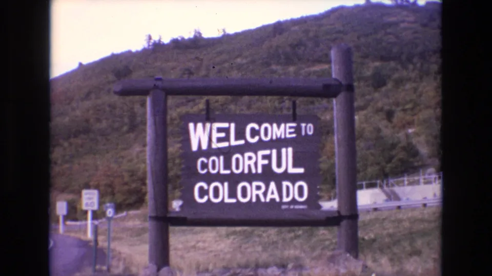 1973 Colorado roadside view with the Welcome to Colorful Colorado sign centered against a wooded slope and highway approach details.