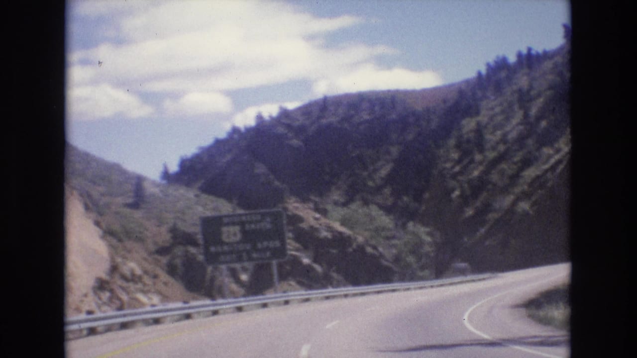 Mountain road curves right past a guardrail and dark roadside sign.