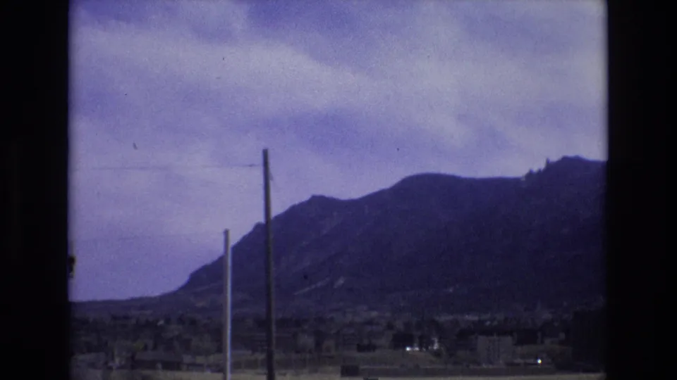 1973 Colorado 8mm frame showing a steady view of a mountain ridge, overcast sky, vertical poles, and sparse development near the base.