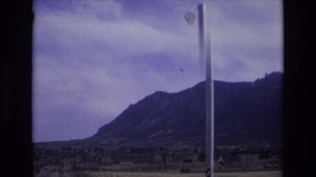 Mountain ridge under cloudy sky with a vertical pole near the center.