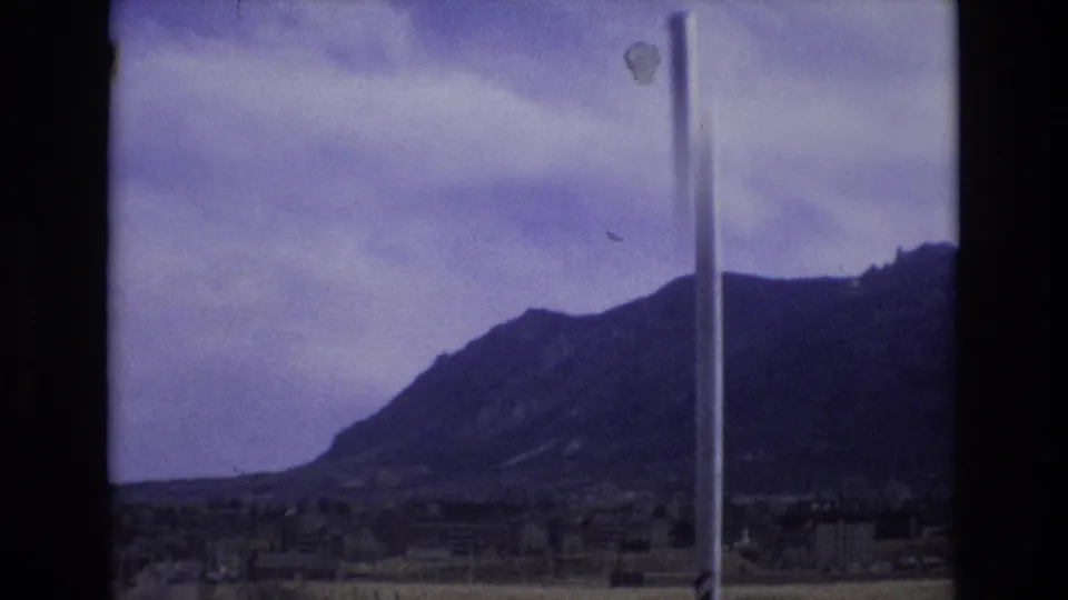 1973 Colorado 8mm frame showing a dark mountain ridge beneath a cloudy sky, partly obstructed by a vertical roadside pole.
