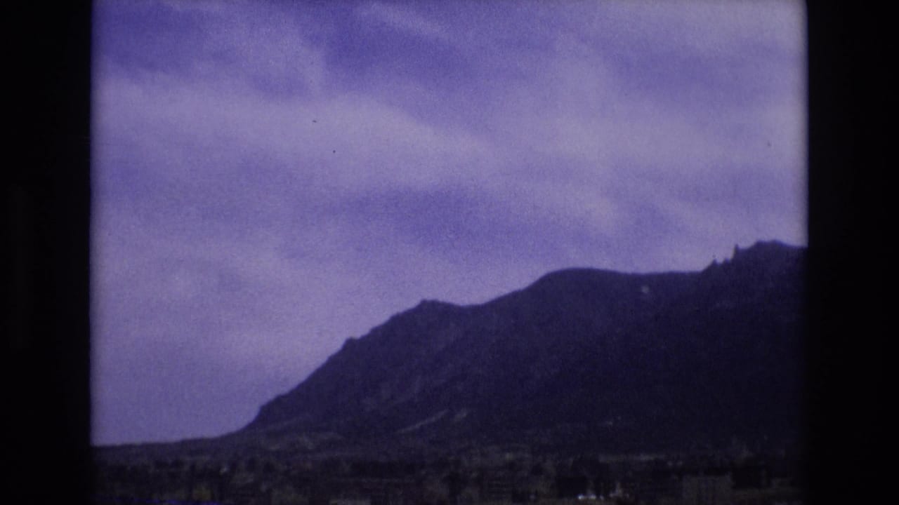 Mountain ridge and cloudy sky seen through a dark film frame border.