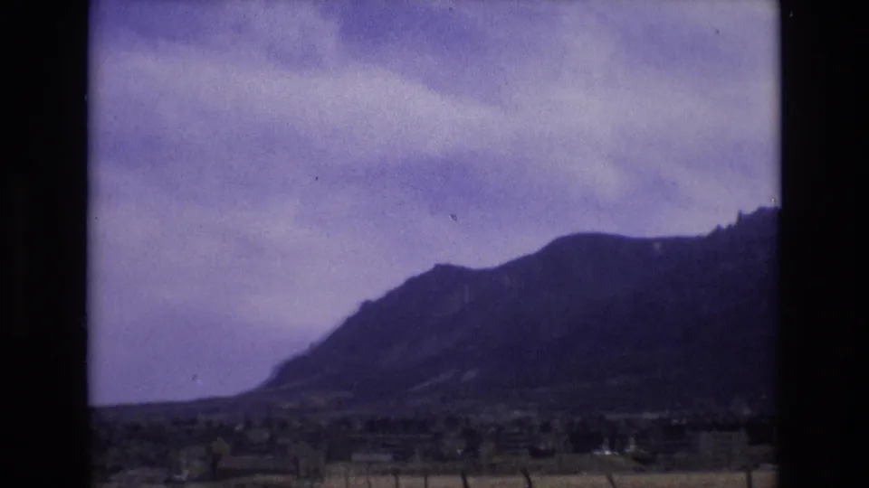 1973 Colorado 8mm frame showing a closer, soft-focus view of a mountain ridge under a cloudy sky from a moving roadside viewpoint.