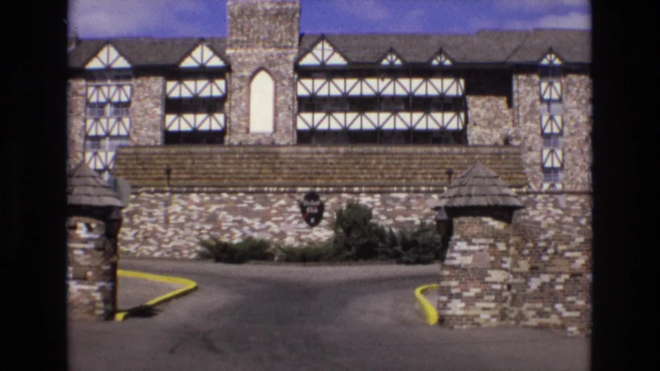 1973 Colorado frame of an exterior hotel or private club entrance, with stone walls, Tudor-style upper facade, yellow curbs, and a small mounted sign visible on the front wall.
