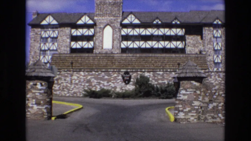 1973 Colorado home-movie frame looking through the entrance toward the stone and half-timbered Oxford Club building, with the driveway and wall sign visible.