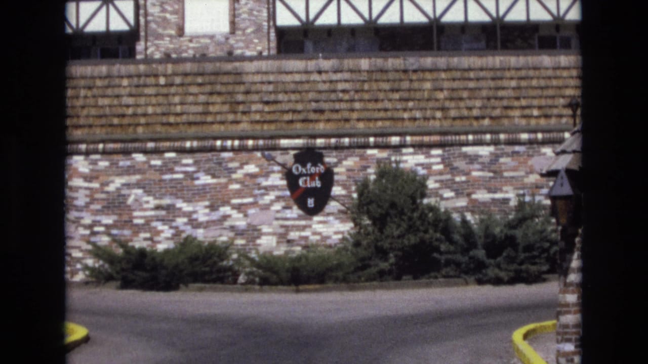 Stone-and-timber building exterior with an Oxford Club sign and shrubs beside a parking area.