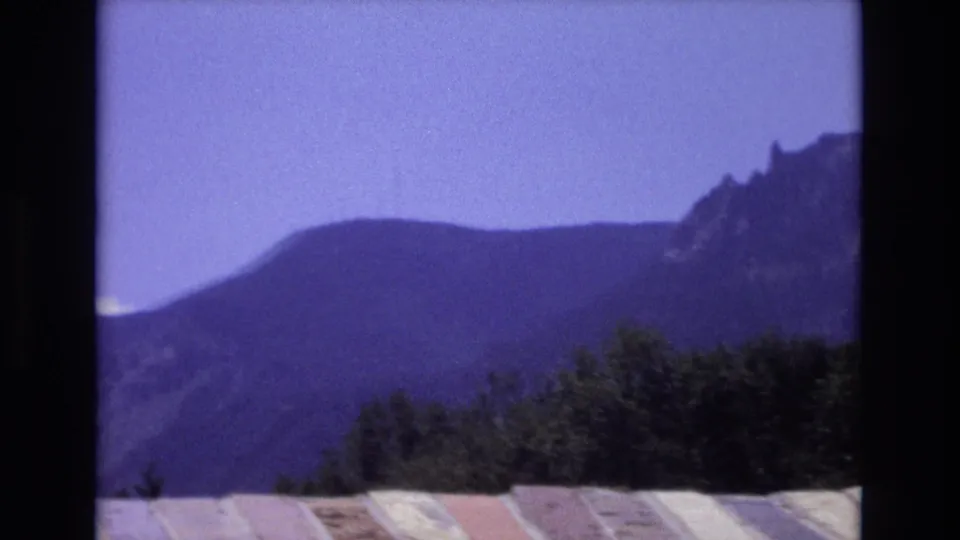 1973 Colorado 8mm frame showing a rounded mountain ridge, darker trees in the foreground, and a pale striped fabric or awning-like edge along the lower frame.